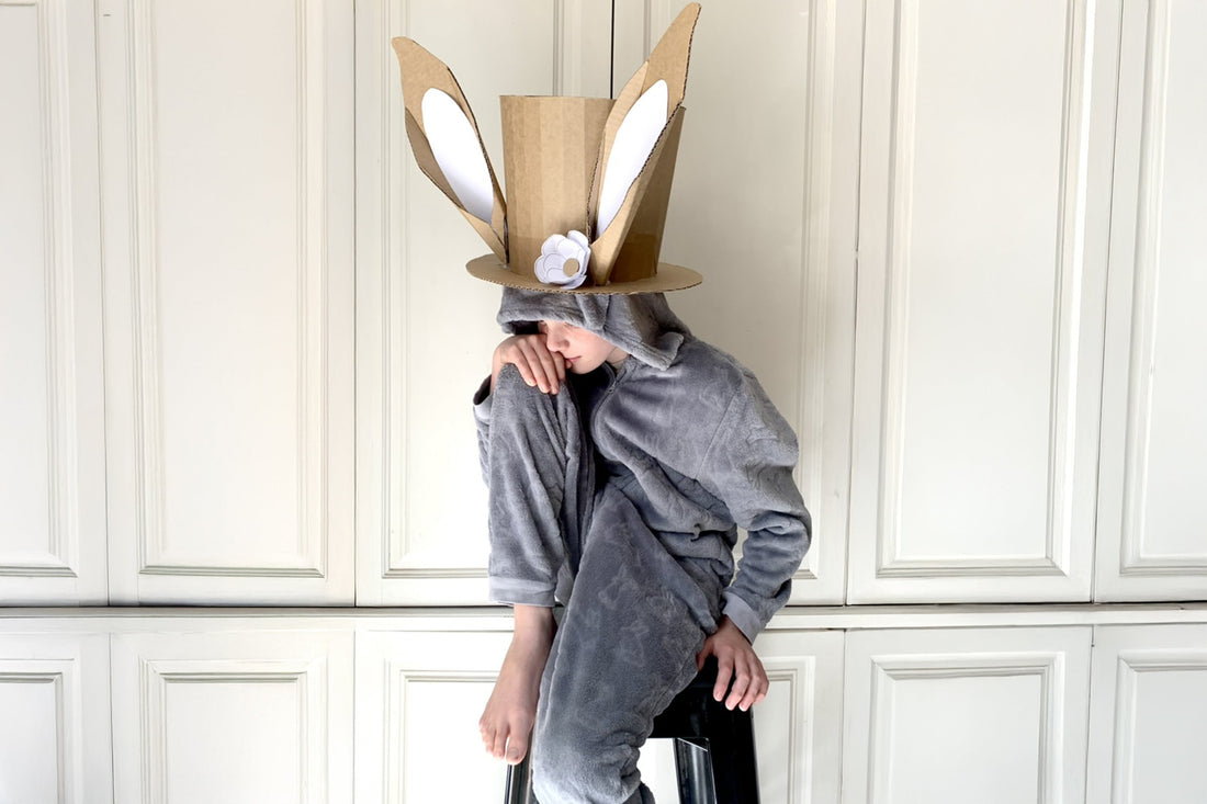 Child sitting on a stool wearing a homemade cardboard bunny top hat.