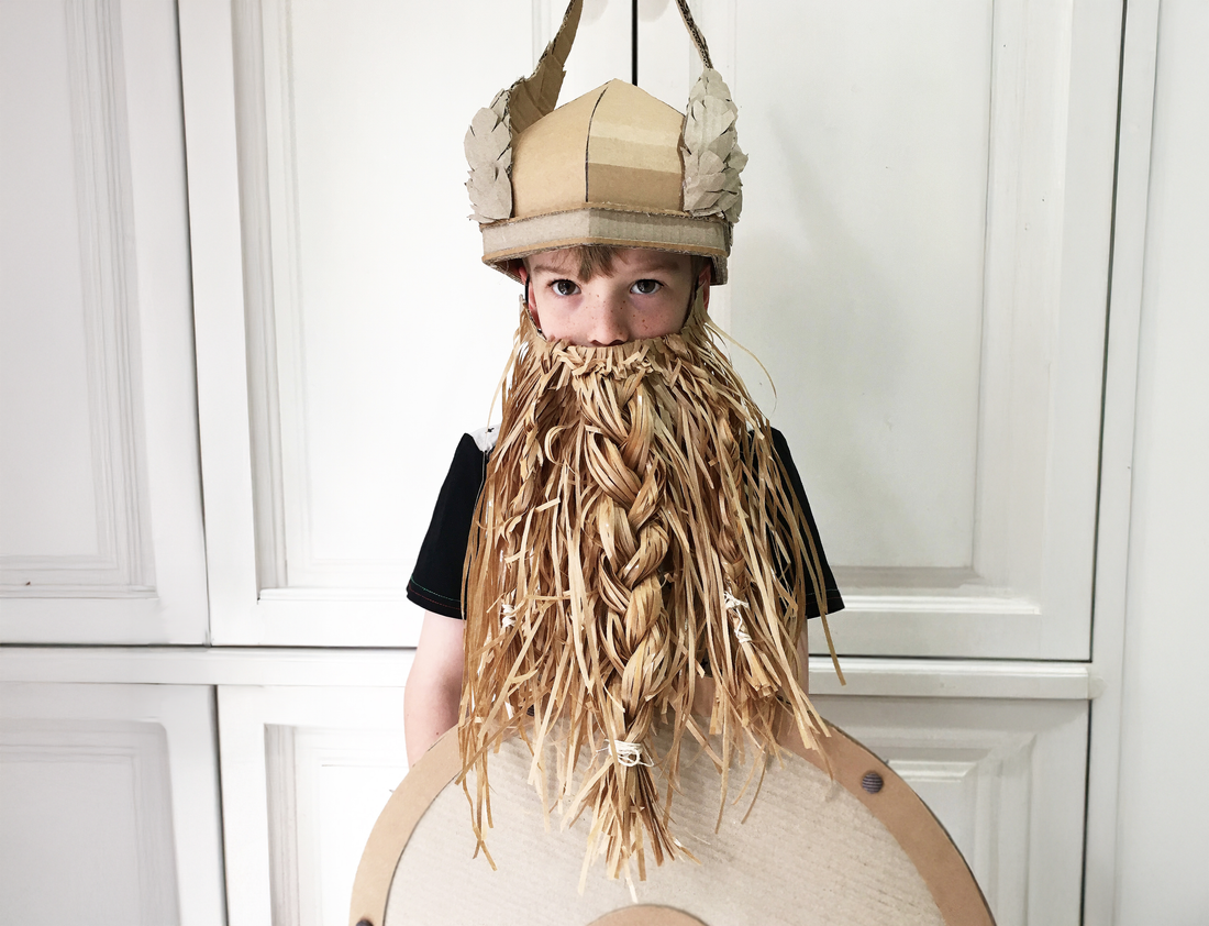 Boy standing dressed as a viking with a Cardboard helmet with wings a paper beard and cardboard shield.