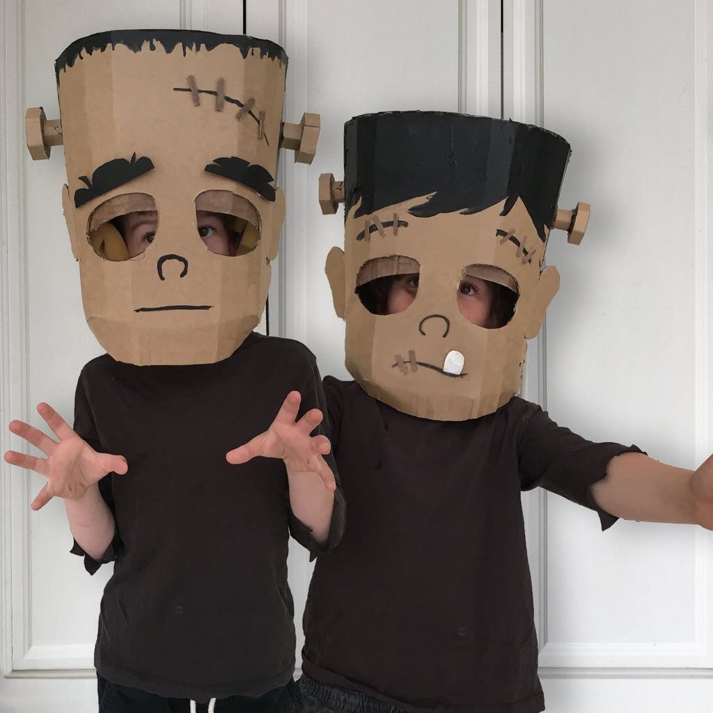 Two children wearing homemade Frankenstein masks against a white paneled background.