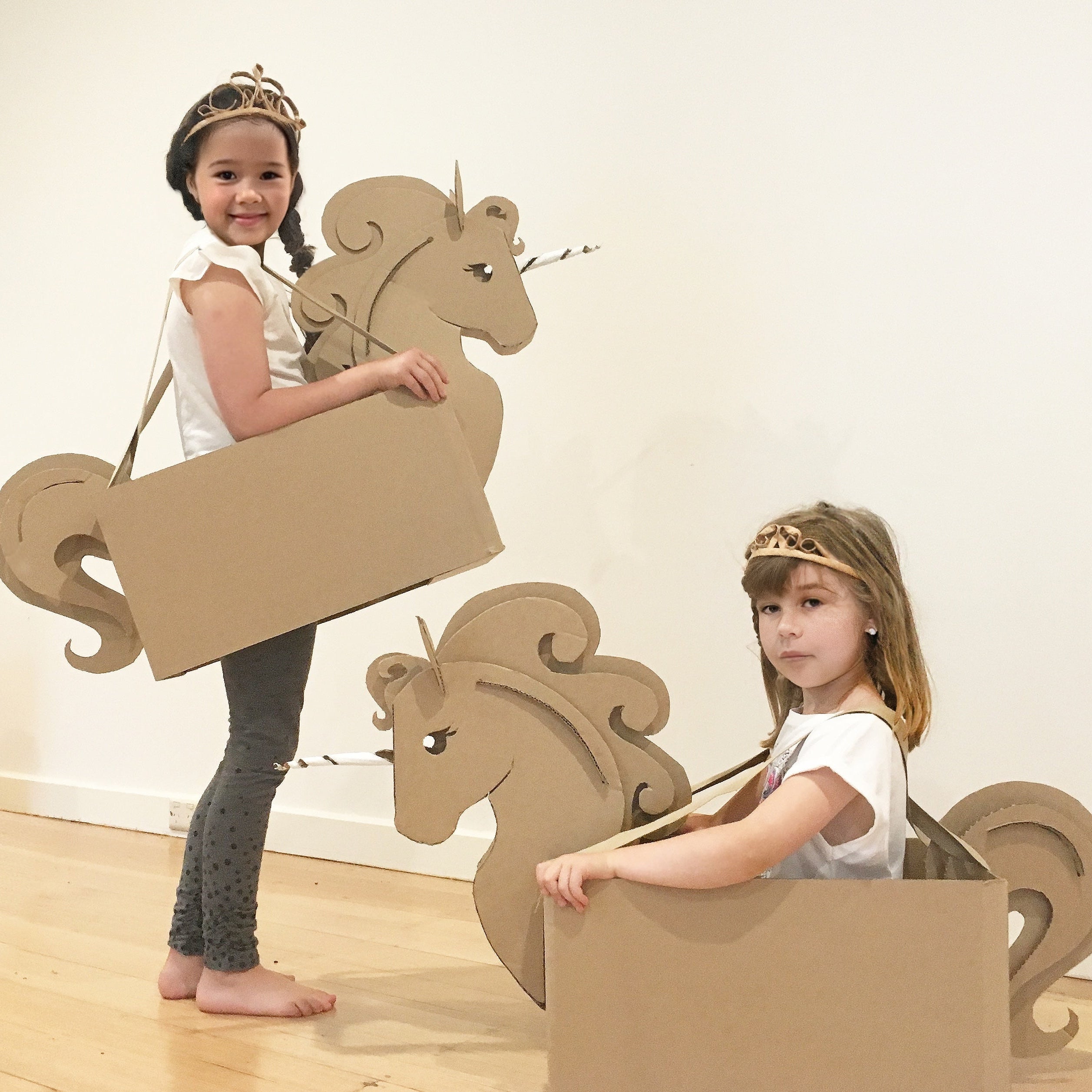 Two children playing with cardboard unicorn box costumes.