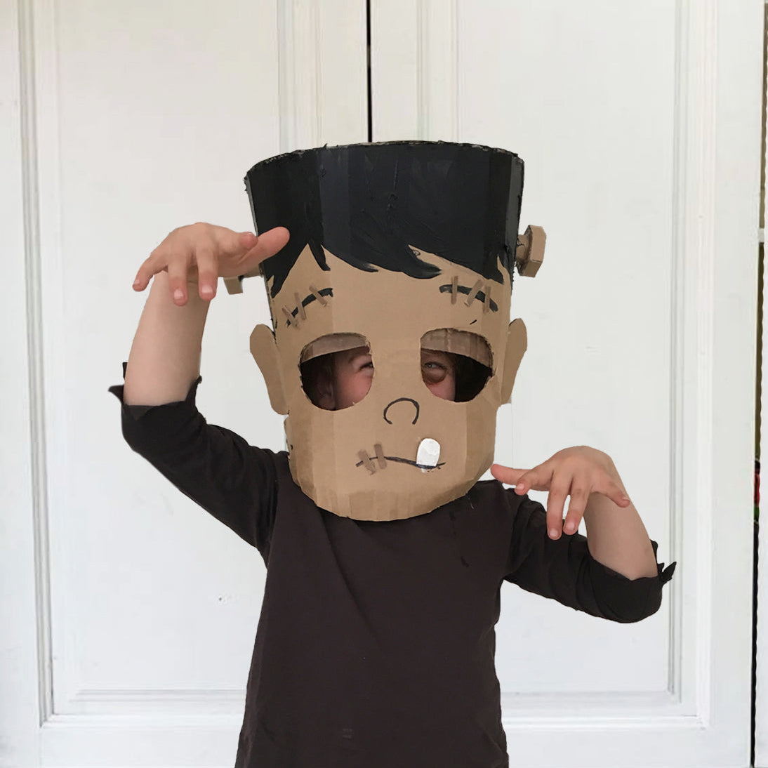 Child wearing a Cardboard Frankenstein monster mask against a white background